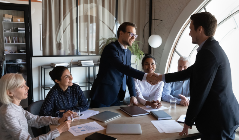 image of team at a table with two co-workers shaking hands